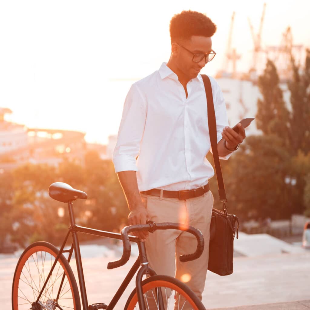 Everyday tech moments – man checking smartphone beside bicycle in warm urban setting