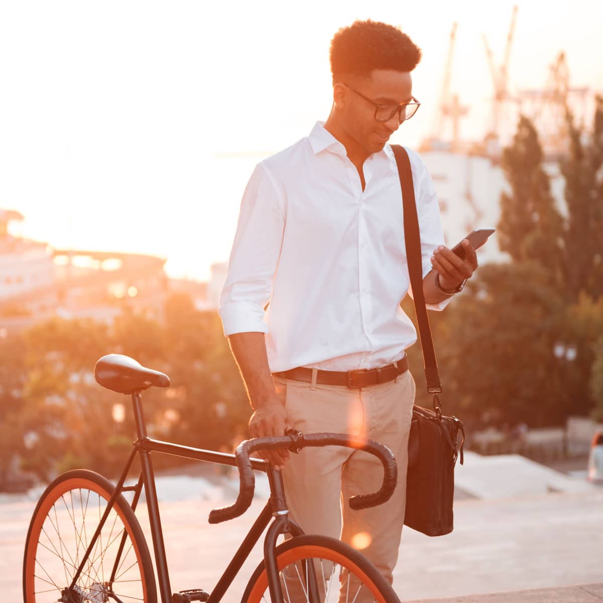 Everyday tech moments – man checking smartphone beside bicycle in warm urban setting